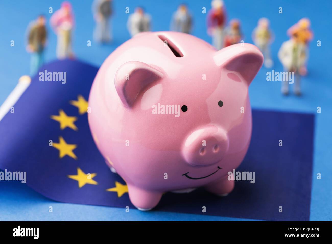 Piggy bank, EU flag and plastic toy people on a colored background, the concept of income in the European Union Stock Photo