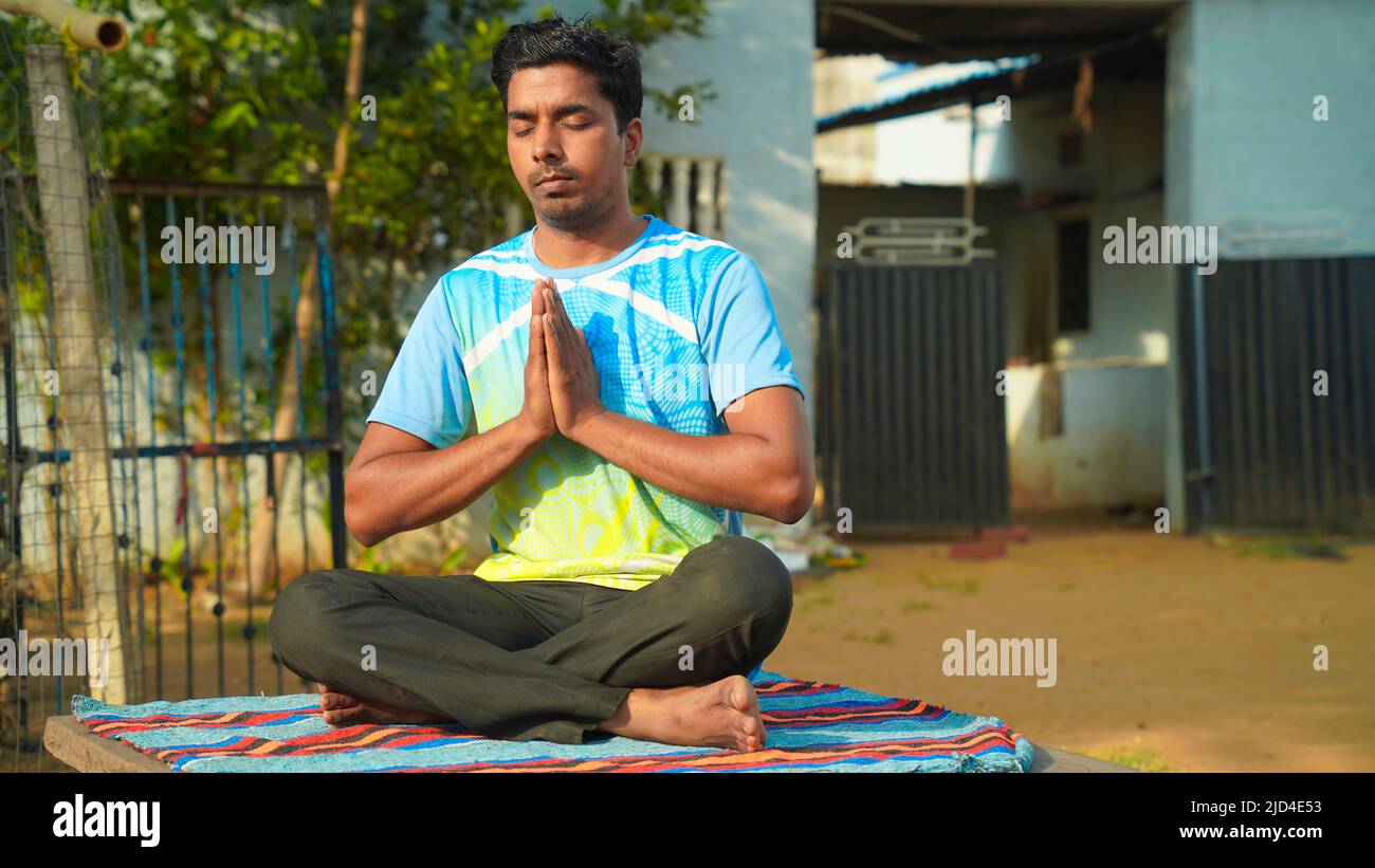 young fit man wearing sportswear meditating, breathing, sitting with crossed legs in Half Lotus Posture at home. Stock Photo