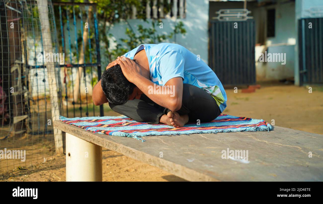 Good looking man in blue sport shirt and black pants sitting on yoga mat doing maditation with hand Stock Photo