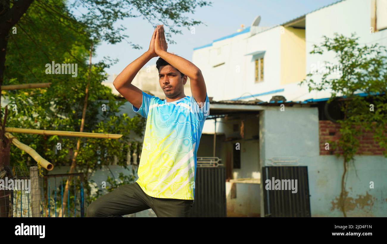 Indian man practices balance yoga asana Vrikshasana tree pose at outdoor. Stock Photo