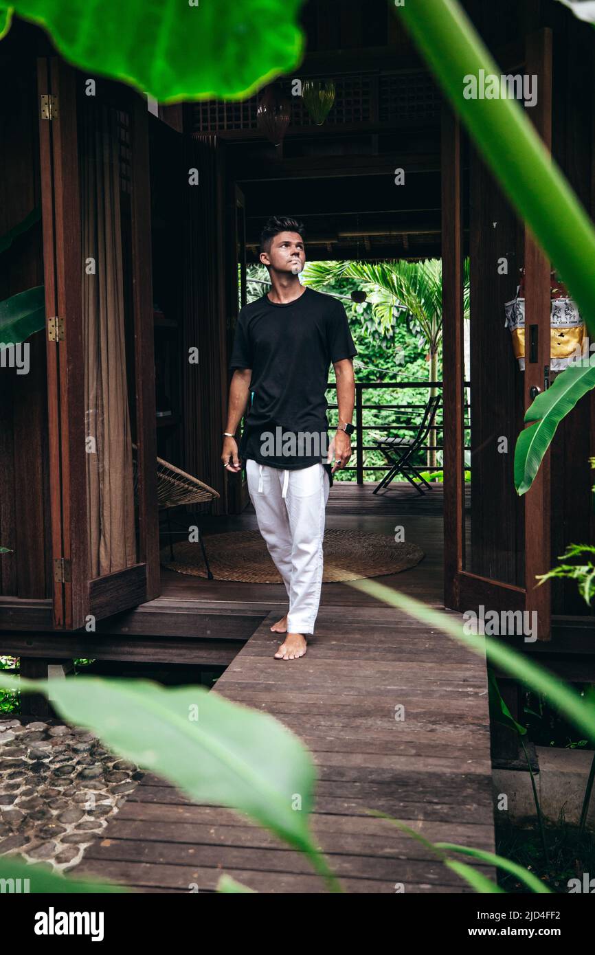 young man walking on wood path from tropical tiny house entryway in bali indonesia Stock Photo