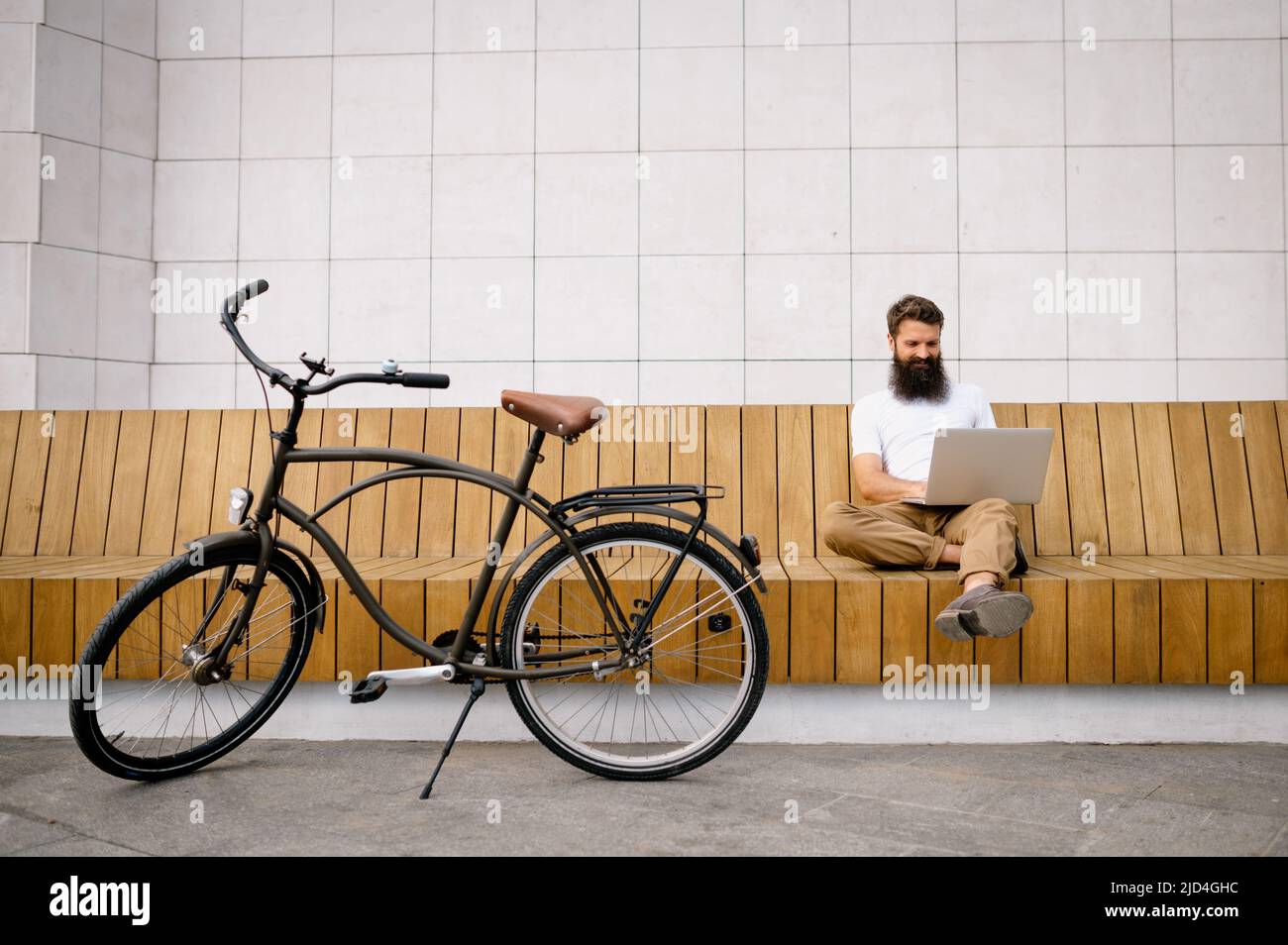 Smiling mid adult man using laptop while sitting on bench Stock Photo