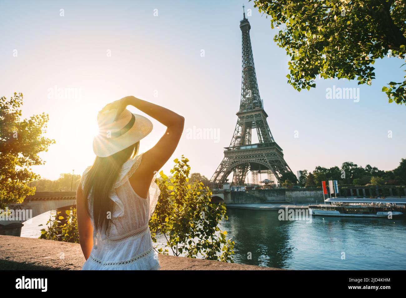 Young woman tourist in sun hat and white dress standing in front of Eiffel Tower in Paris at sunset. Travel in France, tourism concept Stock Photo