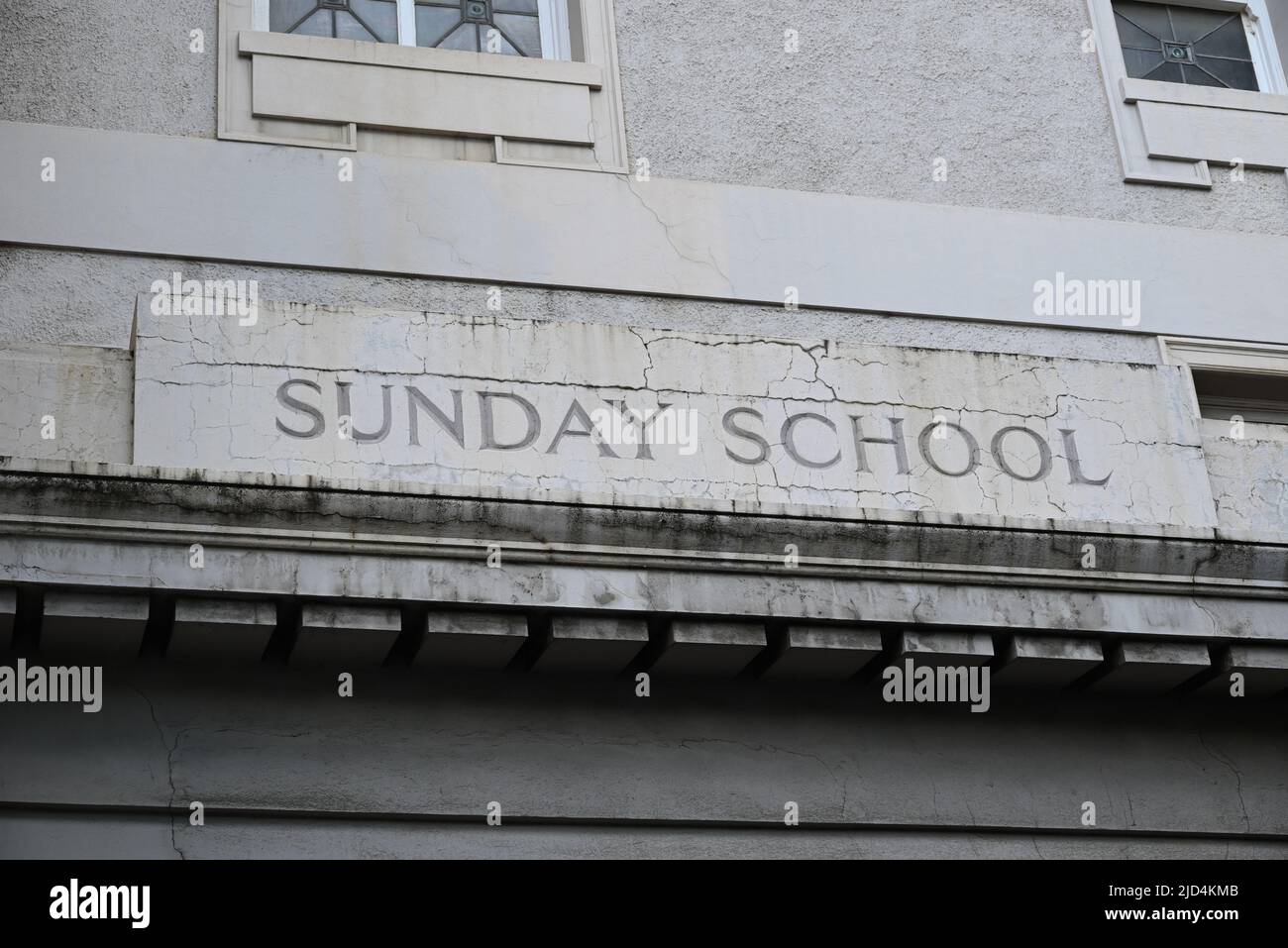 Sunday School sign, surrounded by cracks, engraved in the worn white wall of an old building Stock Photo