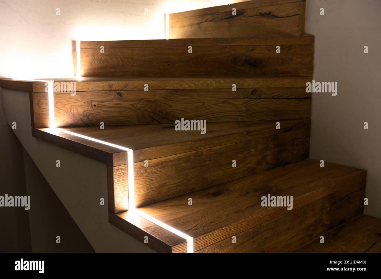 Close-up of Staircase at Home Illuminated with LED Strip Lights. Stairway Lighting Design on Wooden Residential Stairs. Stock Photo