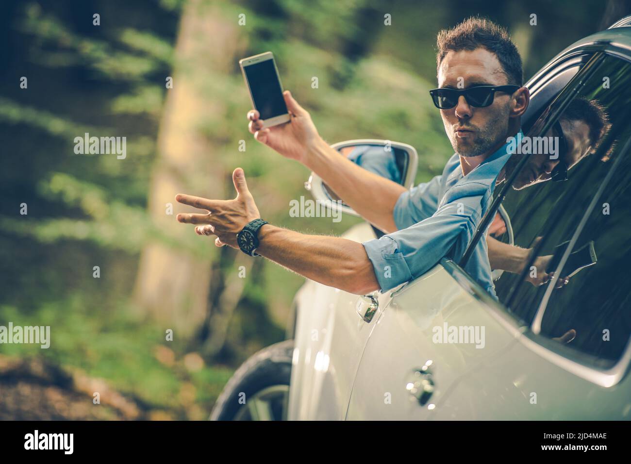 Caucasian Male Driver at His 40s with Phone in a Hand Nervously Looking Backwards Out of His Car Window and Expressing Emotions with Gestures. Stock Photo