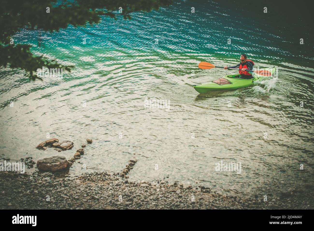 Caucasian Kayaker in His Green Canoe Finishing His River Trip Heading to Stony Shore. Watersport and Recreation Theme. Stock Photo