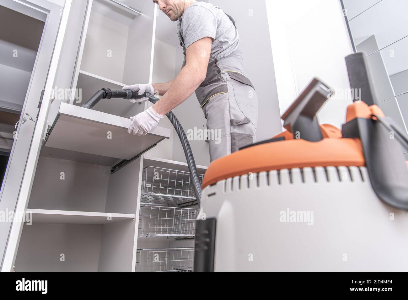 Caucasian Male Worker Vacuuming Shelf in Newly Assembled Large Wardrobe After Finishing the Installation Work in Client’s Residential House. Stock Photo