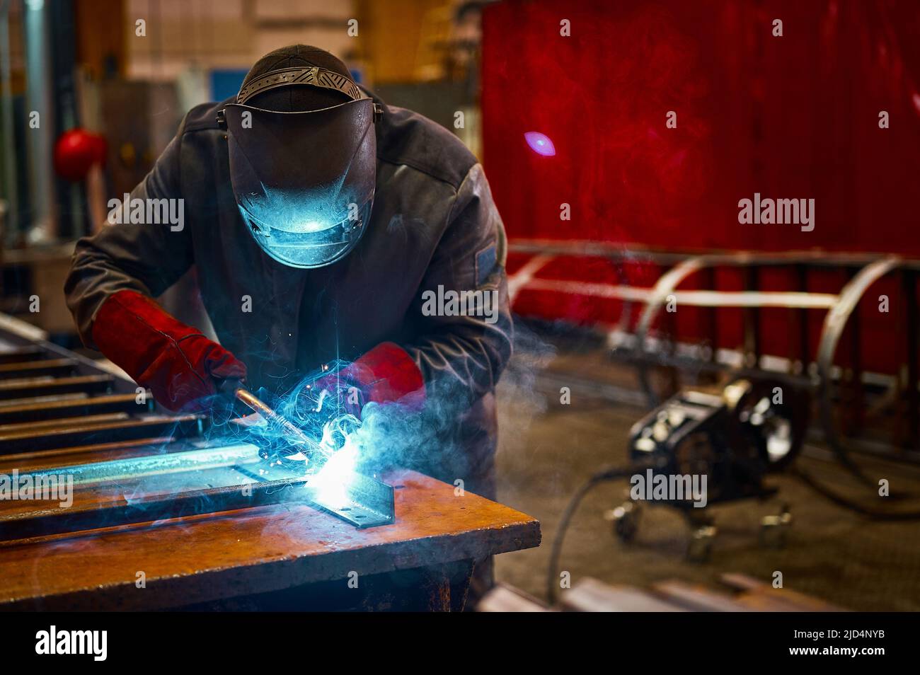 Skilled worker in protective mask welds metal part at plant Stock Photo