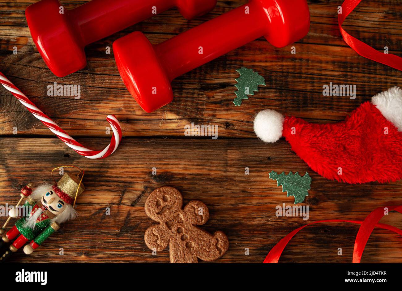 Christmas gym composition concept with dumbbells, candy cane, Santa Claus hat, gingerbread man cookie, tree ornaments and nutcracker figure. Stock Photo