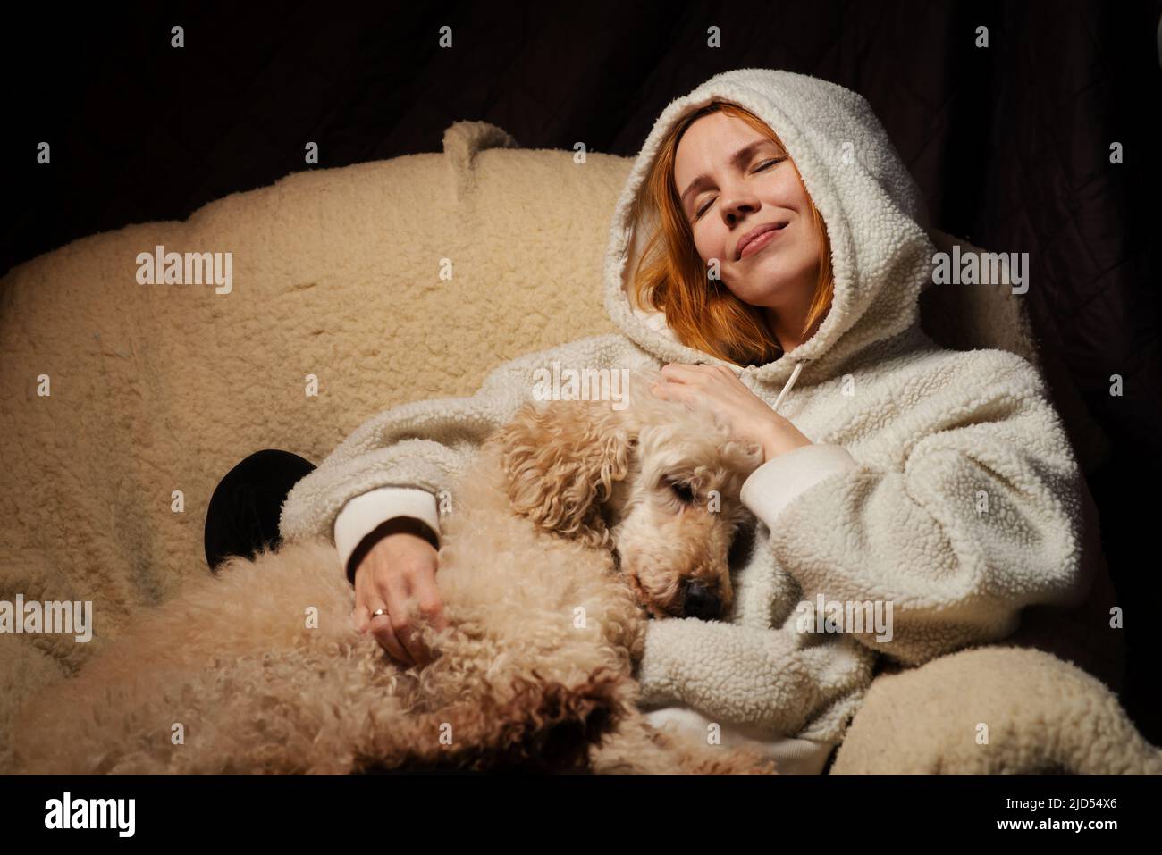 woman lies with a large dog on the couch. The shaggy domestic dog laid its head. The relationship of animals and people at home. Stock Photo