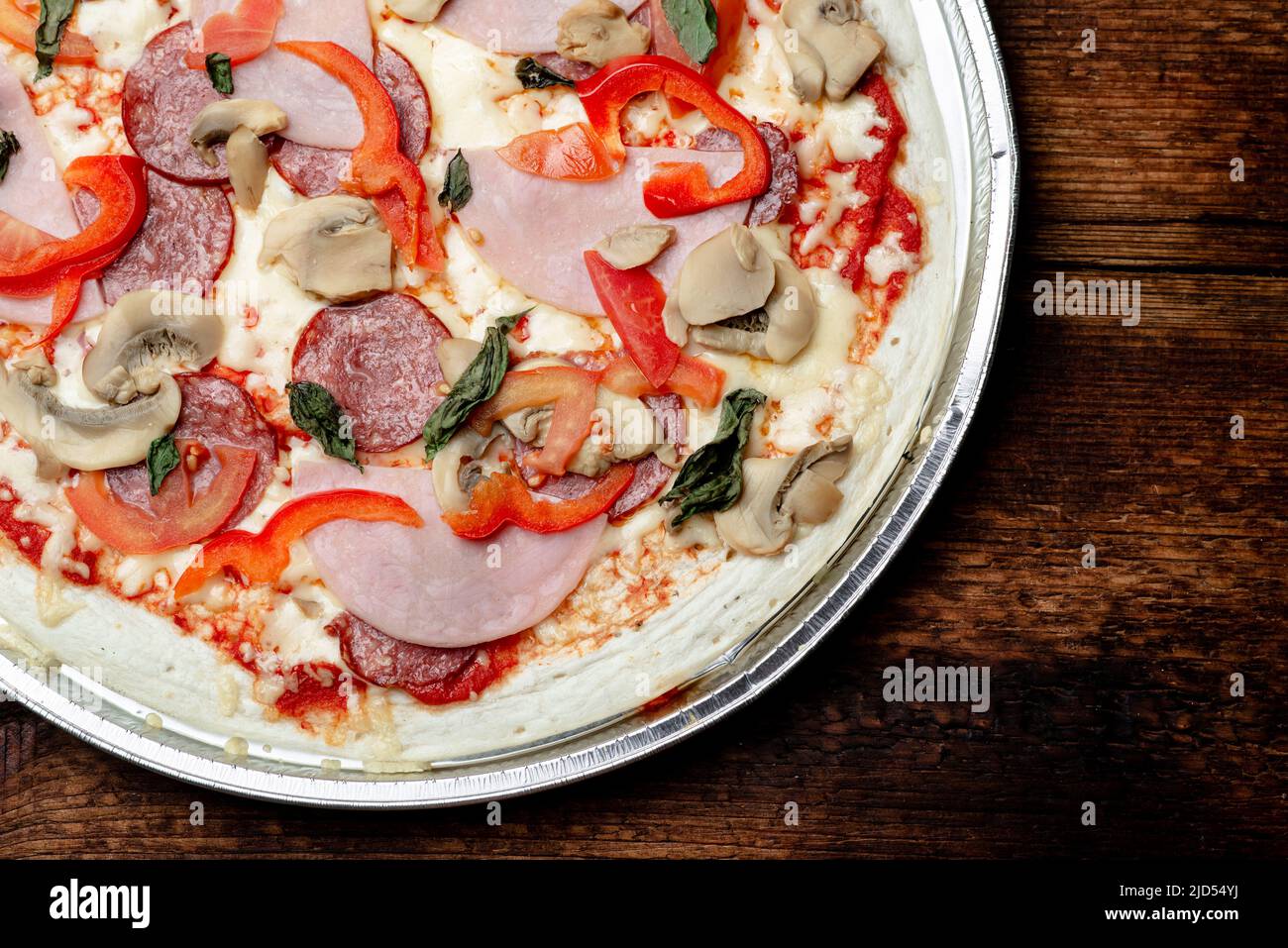 Pizza edge closeup on a wooden background. Bacon, salami, mushrooms and
