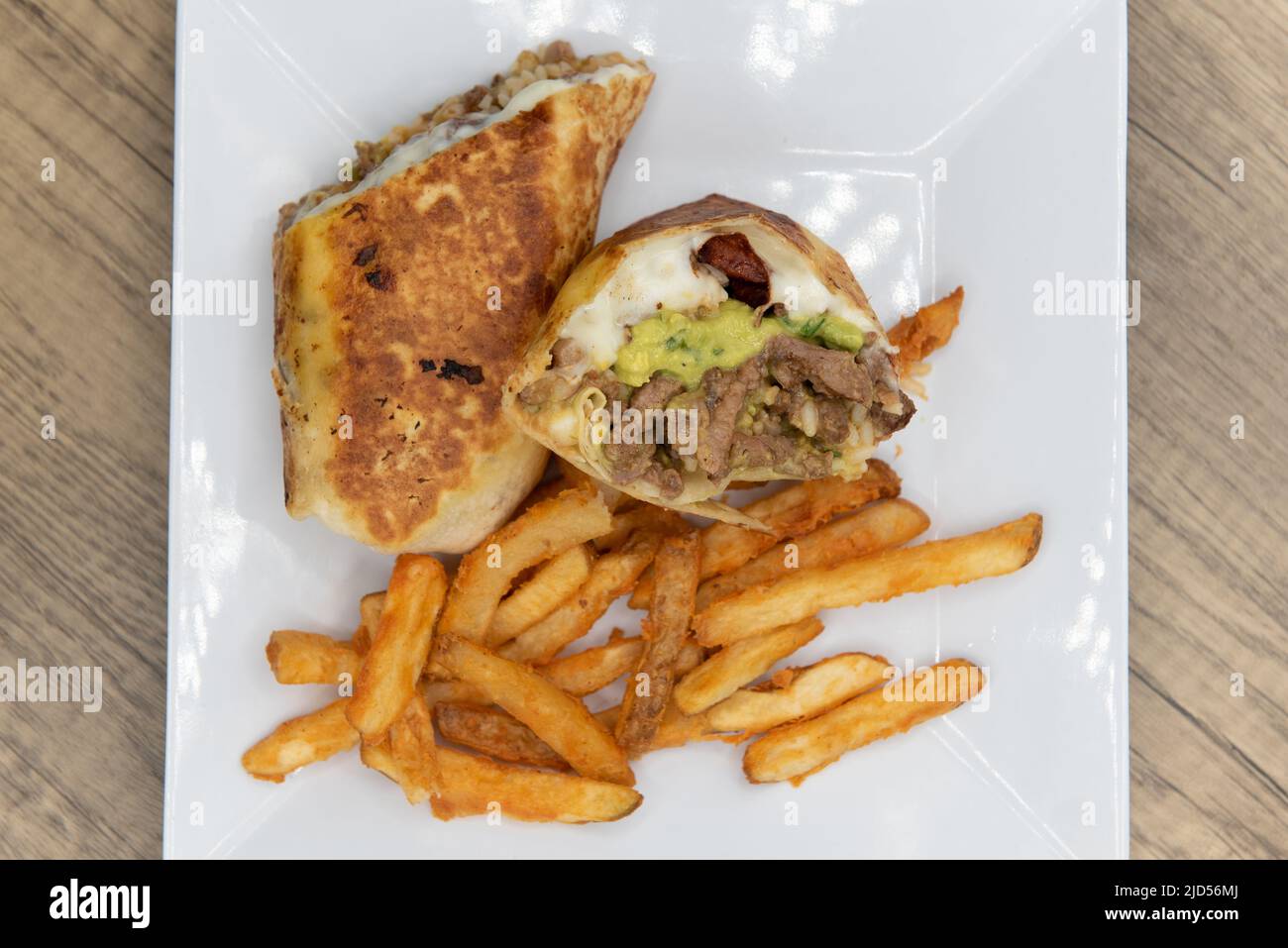 Overhead view of appetizing carne asada steak burrito cut in half and served with french fries for a tempting Mexican food delicacy. Stock Photo