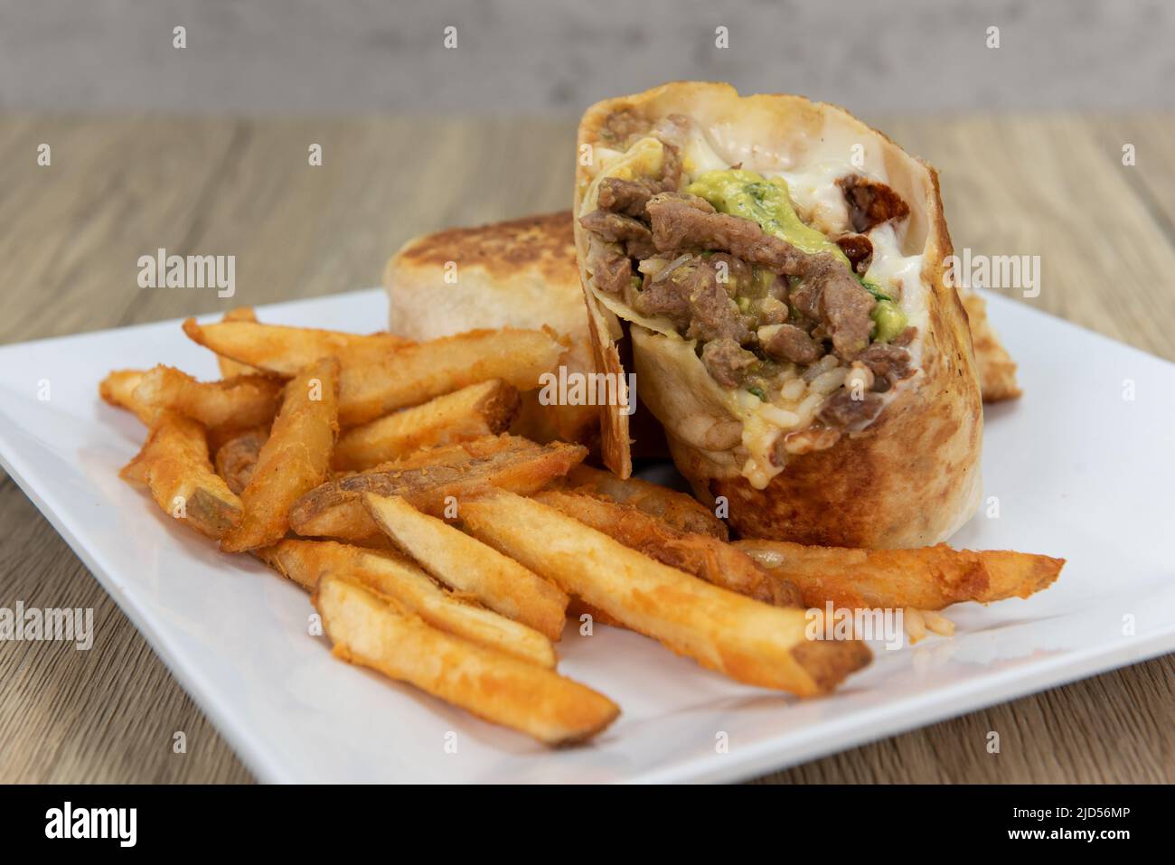 Appetizing carne asada steak burrito cut in half and served with french fries for a tempting Mexican food delicacy. Stock Photo