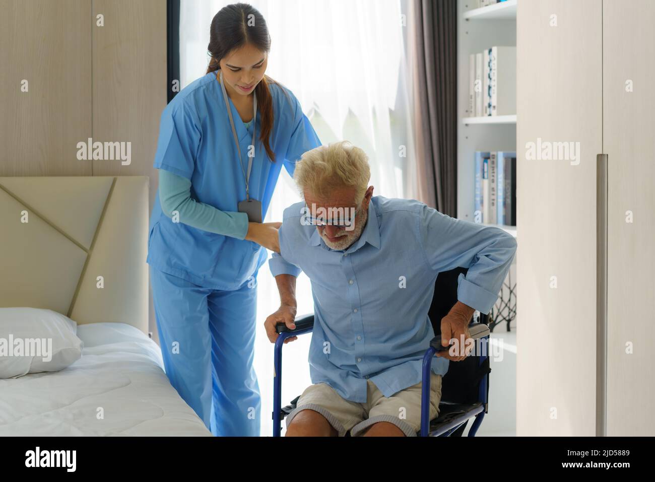 Asian smiling nurse helping senior man get out of bed nursing care support patient while getting out of bed and moving to wheelchair at home helping h Stock Photo