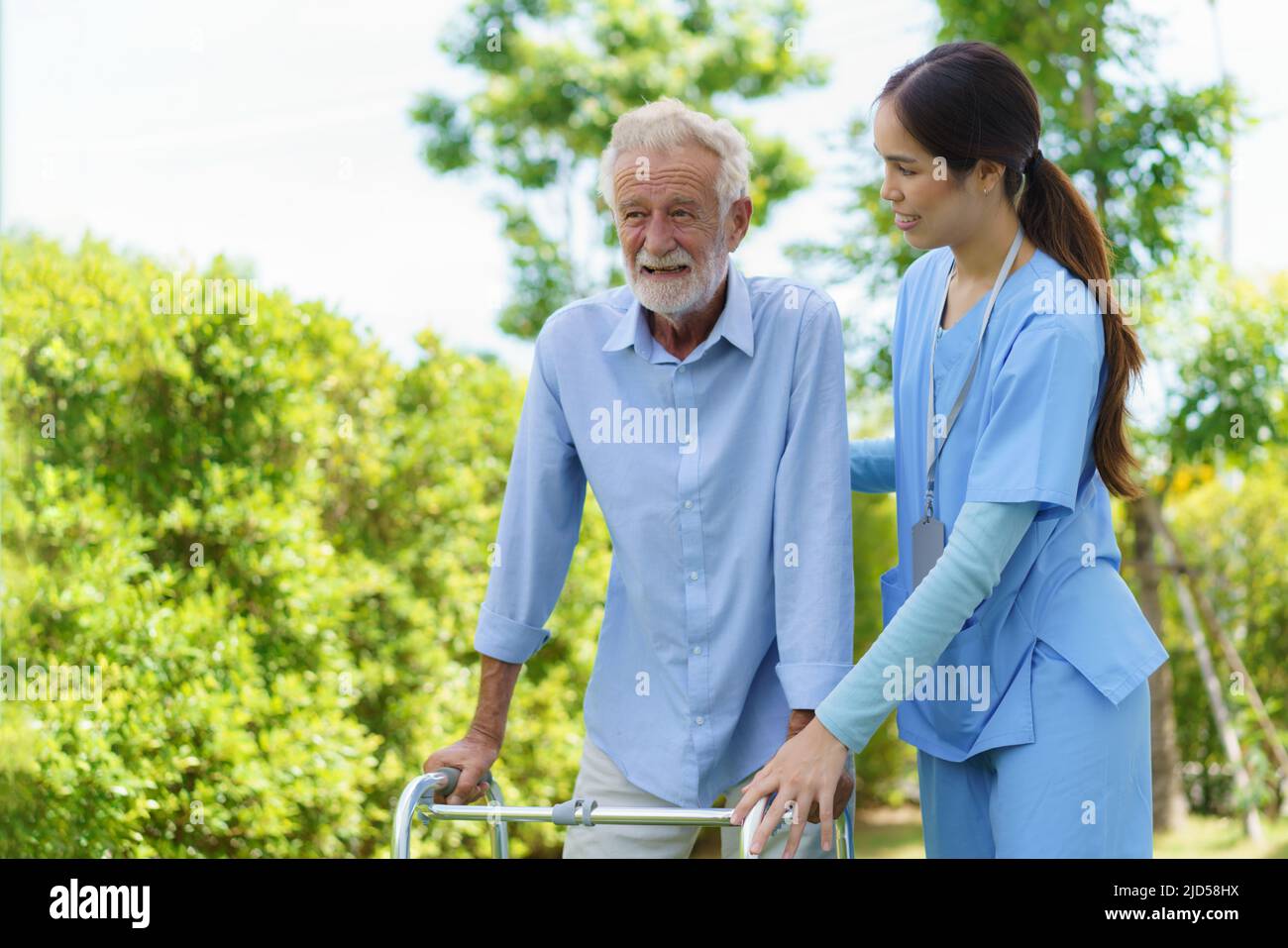 Young Asian woman nurse care giver helping senior old man with mobility walker in garden at home. Senior daycare center, Nurse take care elderly patie Stock Photo