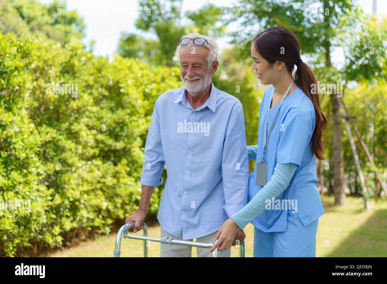 Young Asian woman nurse care giver helping senior old man with mobility walker in garden at home. Senior daycare center, Nurse take care elderly patie Stock Photo