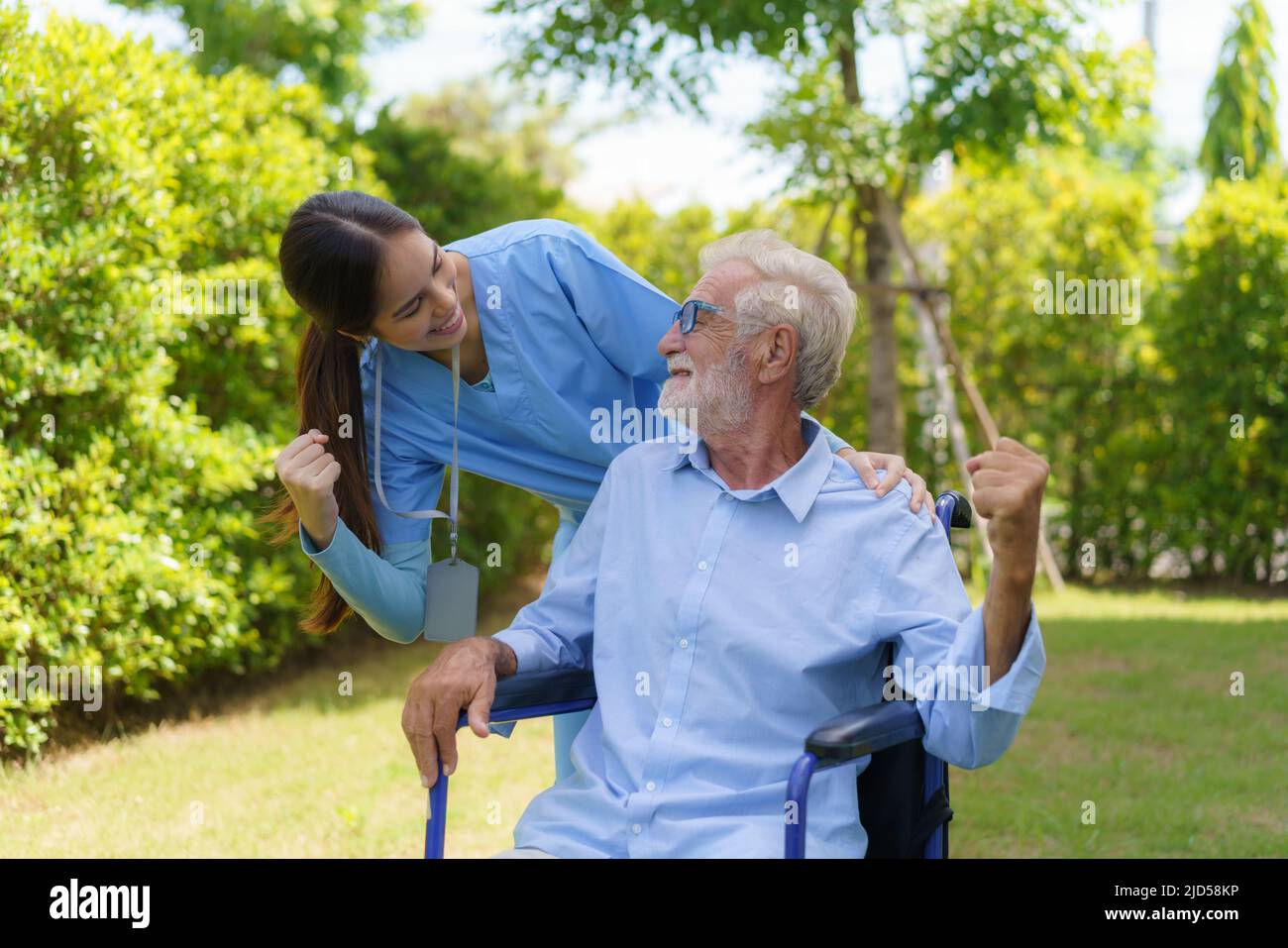 Asian nurse sitting on a hospital bed next to an older man helping hands care in garden at home. Elderly patient care and health lifestyle, medical co Stock Photo