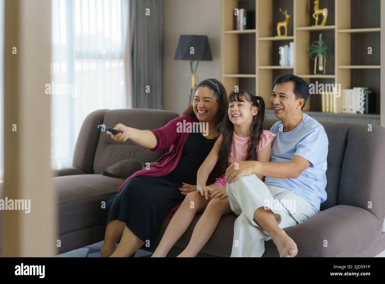 Happy Asian family with father, mother and daughter enjoy weekend activity spending more time at home and therefore probably more time in front of the Stock Photo