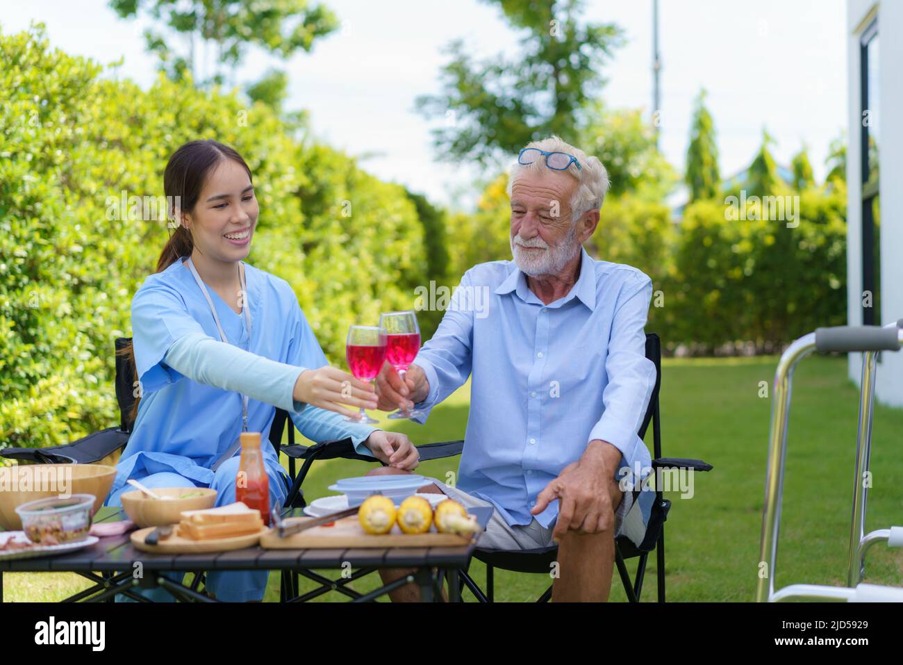 Caucasian handicapped elderly people with mobility walker camping with Asian woman caregivers at home garden to relax and experience nature in the sum Stock Photo