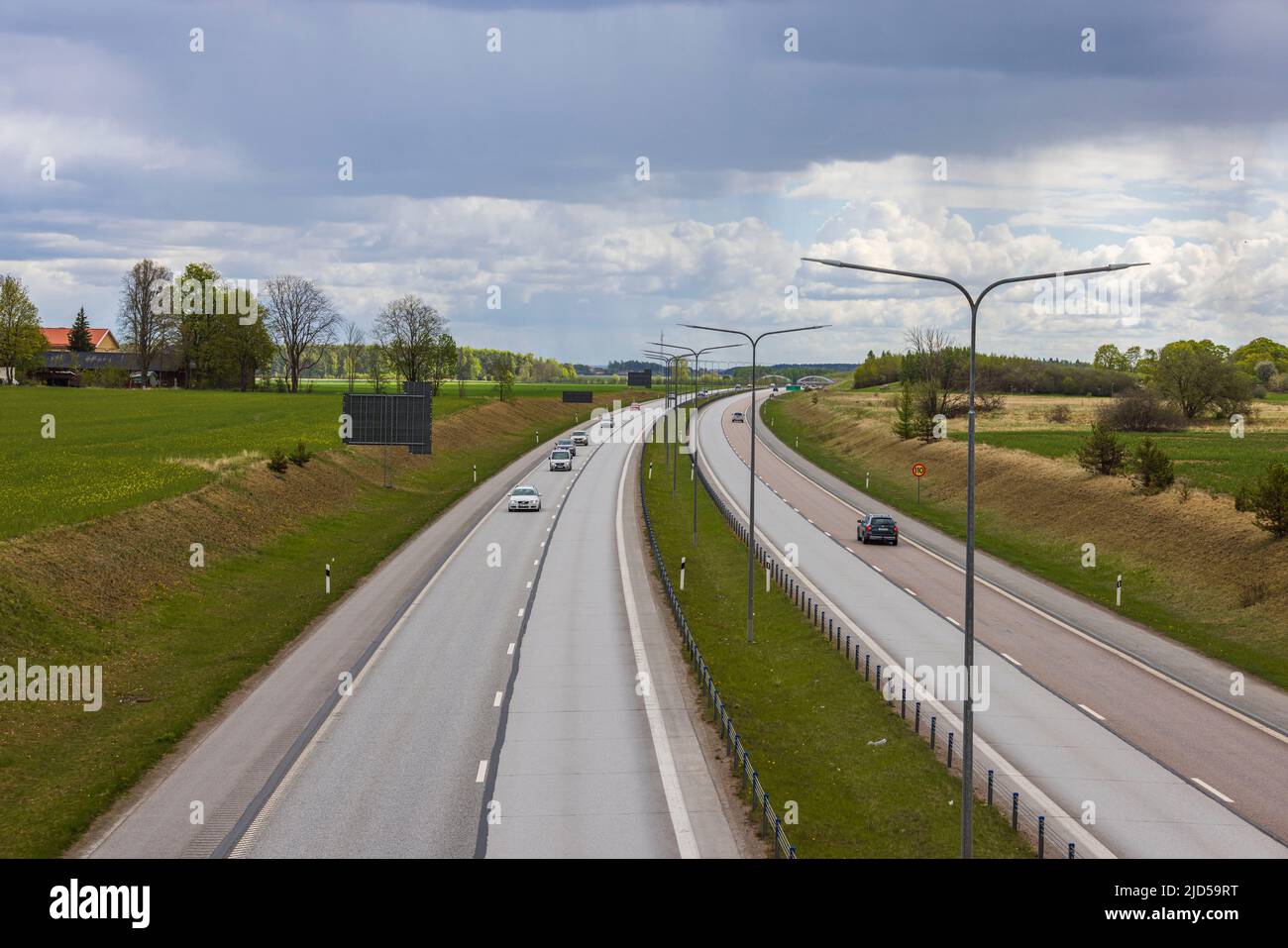 Beautiful top view of highway with several cars. Green side fields and sky with clouds background. Sweden. Stock Photo