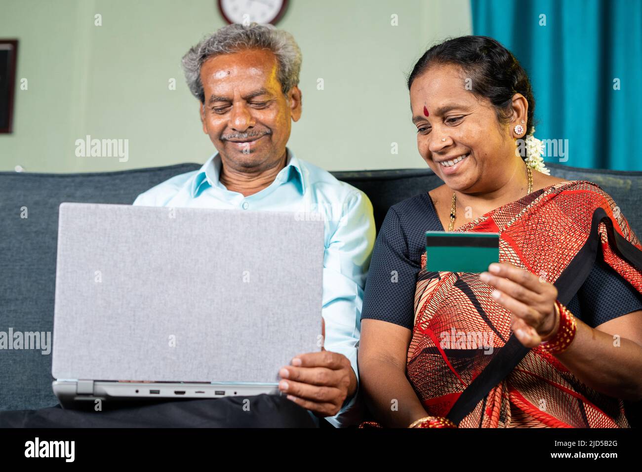 happy senior couple making online payment of e commerce purchase using credit card on laptop at home - concept of shopping, bill payment and banking Stock Photo