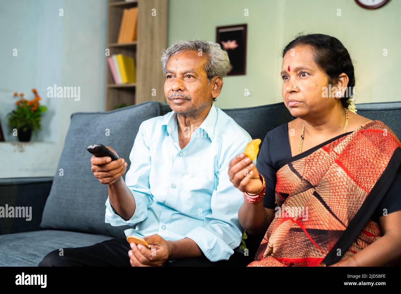 Senior couple at home busy watching tv by surfing channel at home - concept of leisure activities, entertainment and relaxing lifestyle Stock Photo