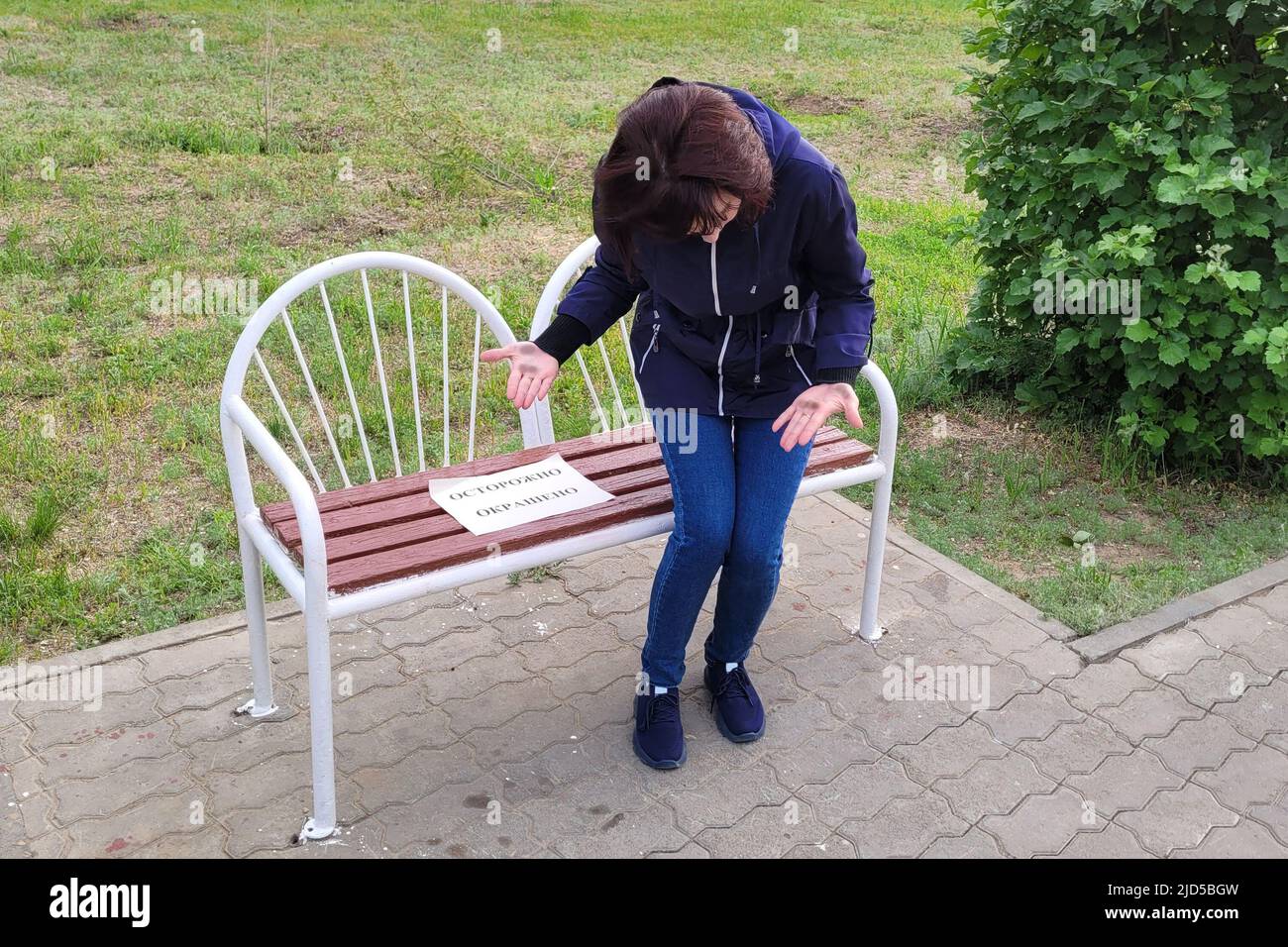 A woman looks with horror her paint stained hands after getting up from a painted bench. The inscription paper is carefully colored. Stock Photo