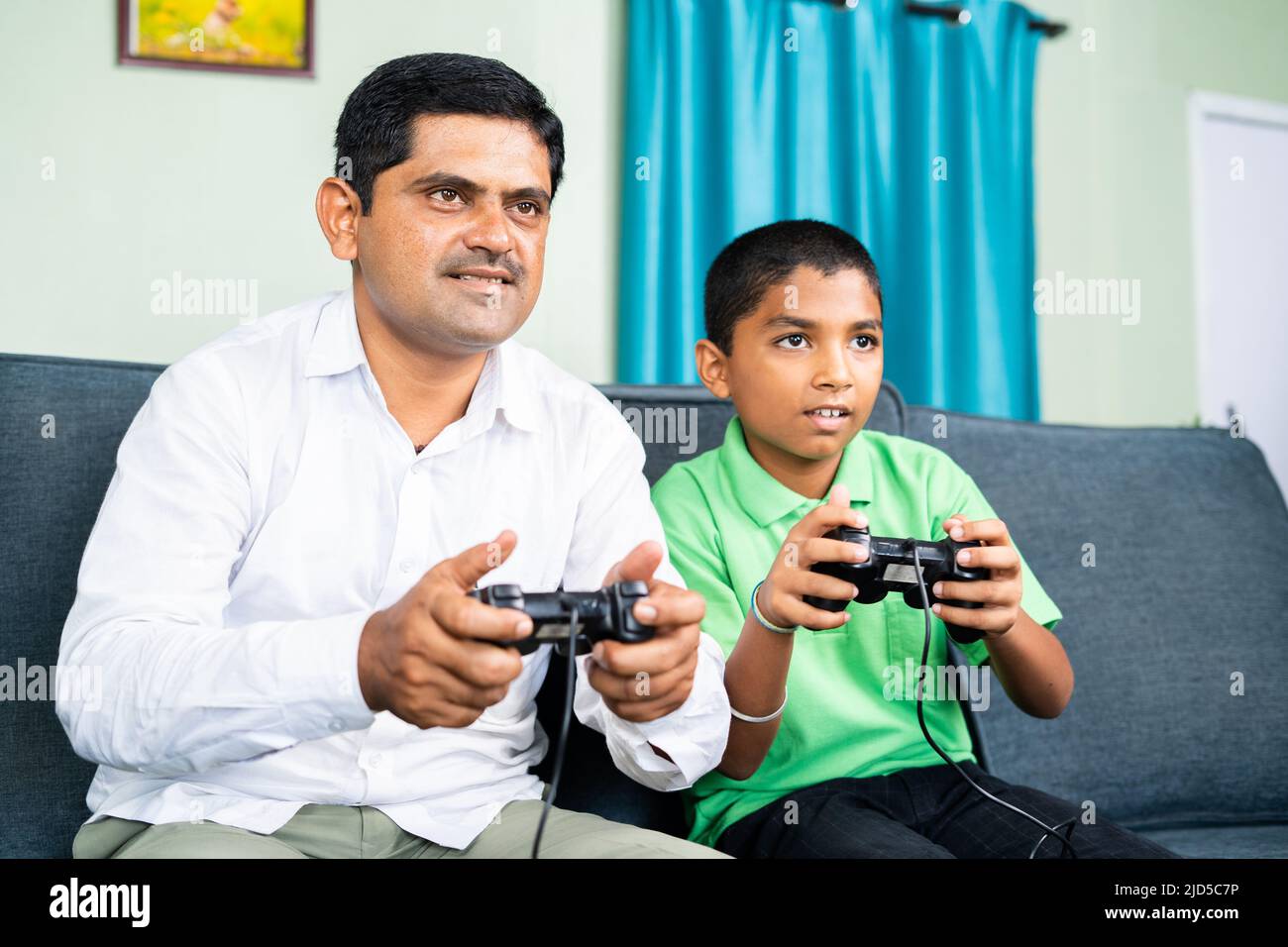 Father and son playing video game using game pad at home during weekend holidays - concept of entertainment, bonding and leisure lifestyle Stock Photo