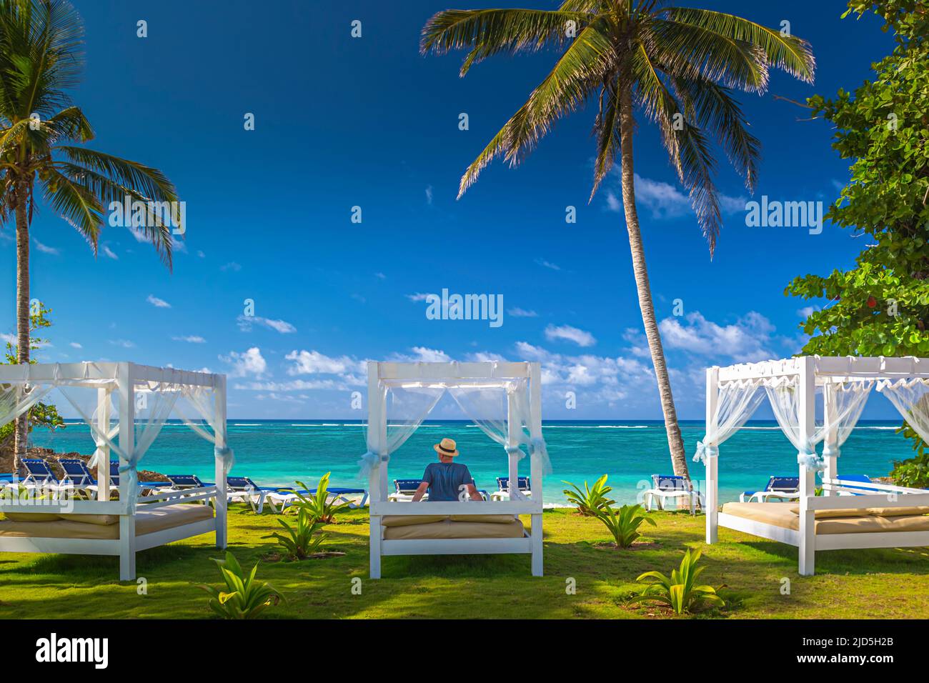 Man enjoys the beautiful view on a daybed at a resort, surrounded by the turquoise blue sea and plan trees near Baracoa, Cuba Stock Photo