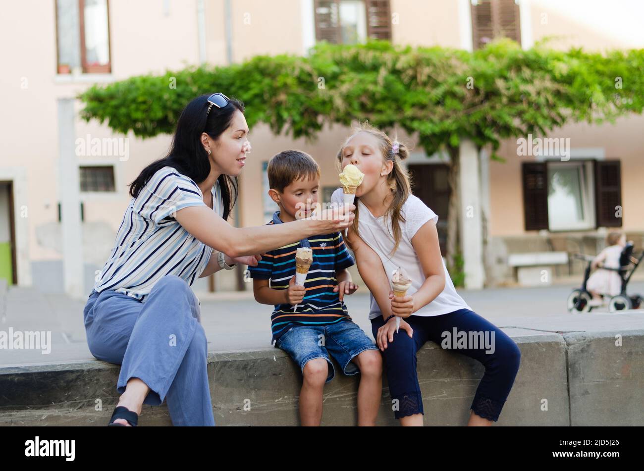 Happy family lifestyle and holiday concept. Mother, little boy, girl sitting, walking in old city, street. laughing on a summer sunny day. Having fun Stock Photo