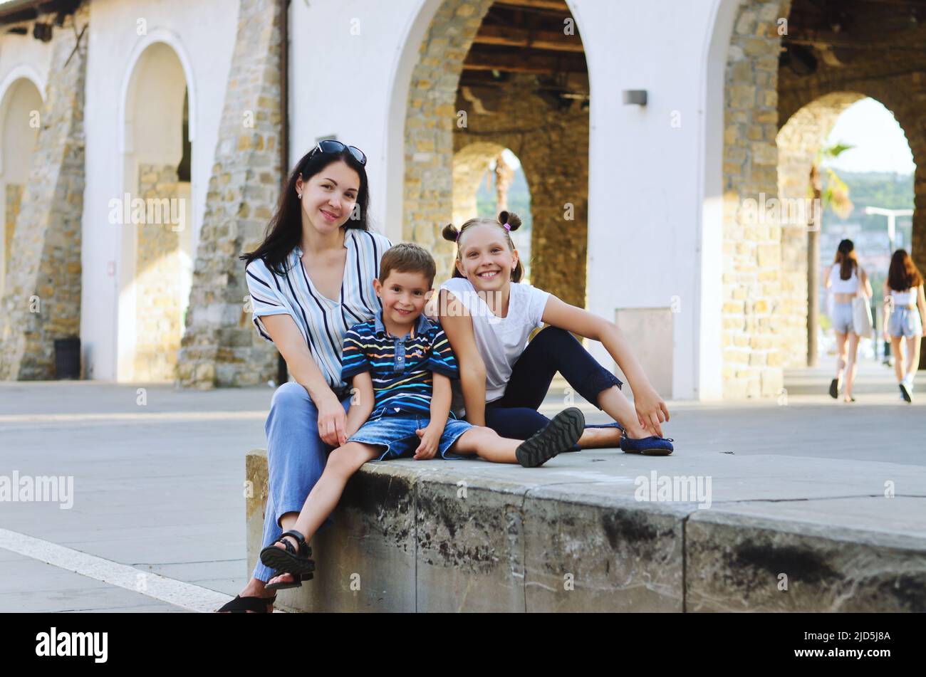 Happy family lifestyle and holiday concept. Mother, little boy, girl sitting, walking in old city, street. laughing on a summer sunny day. Having fun Stock Photo