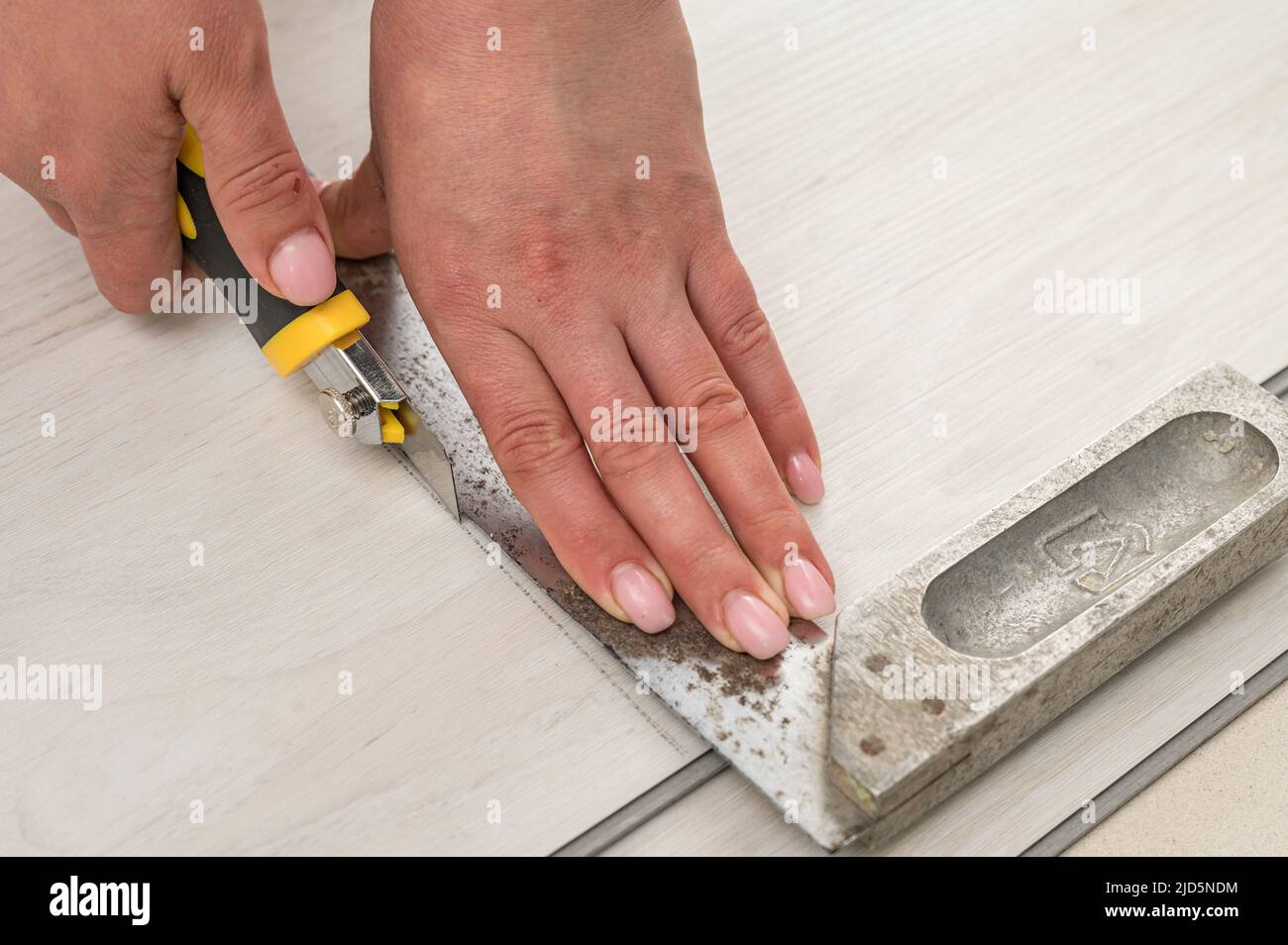 Female master cuts quartz vinyl floor with a stationery knife, floor installation, woman performs repair work. Stock Photo
