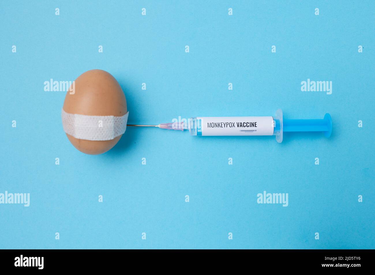 flatlay with monkeypox vaccine syringe and vaccinated egg with medical patch on blue background. Stock Photo