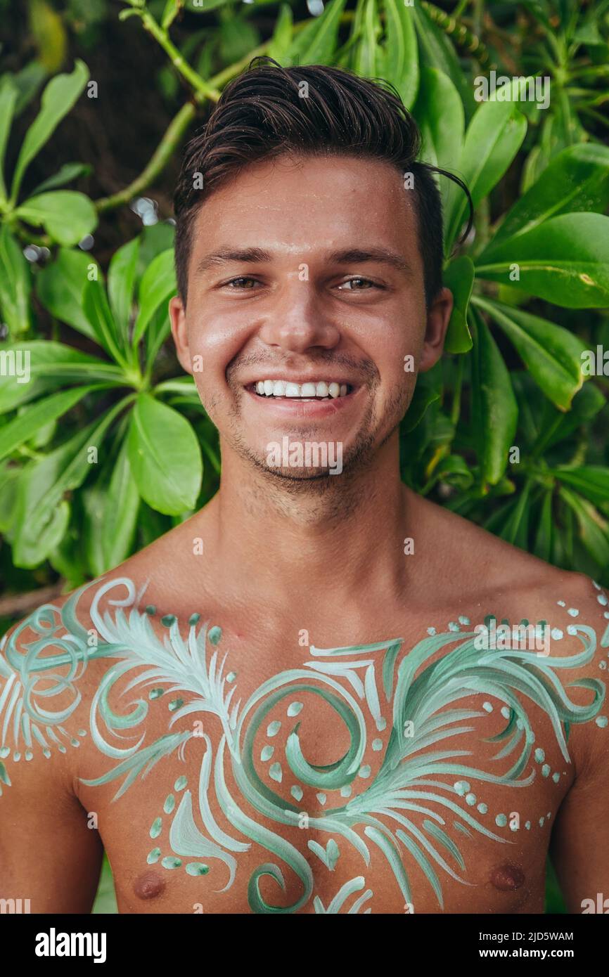 young happy smiling man with green foliage background and beautiful body paint art Stock Photo