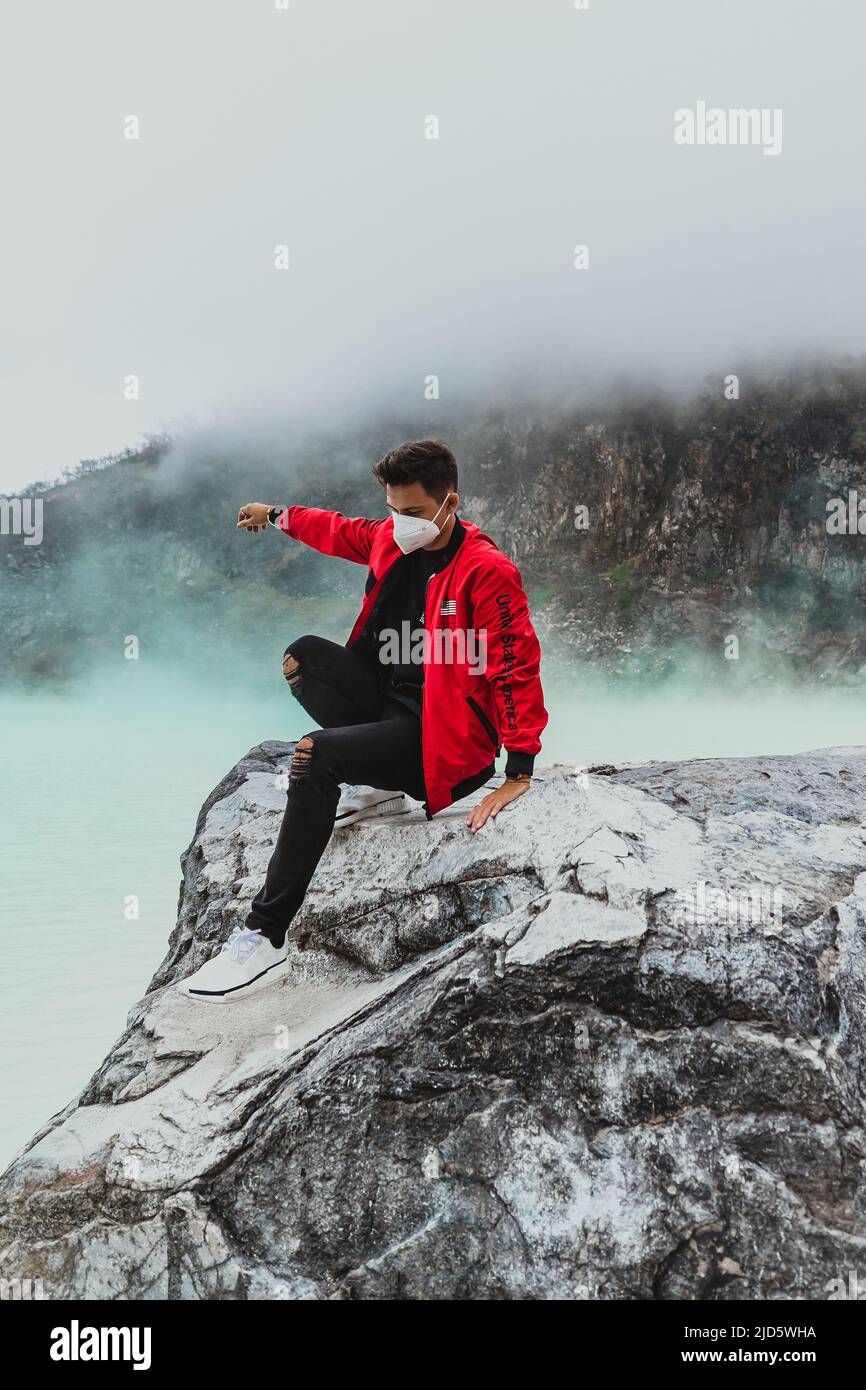 young man in red bomber jacket climbing down from rock at kawah putih