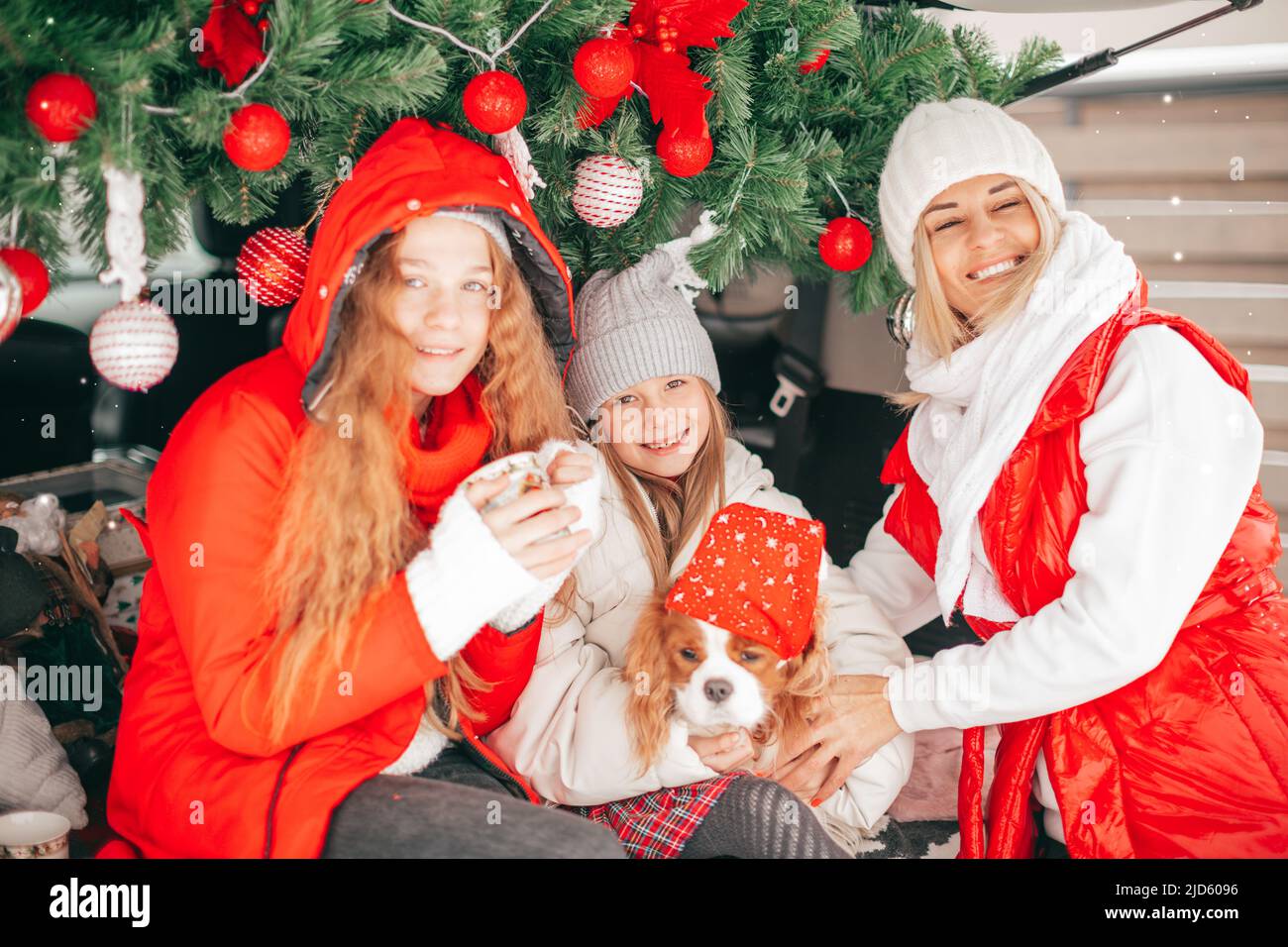 Young happy family in cozy car trunk with holiday decoration on Christmas eve, Mother and daughters have fun Stock Photo