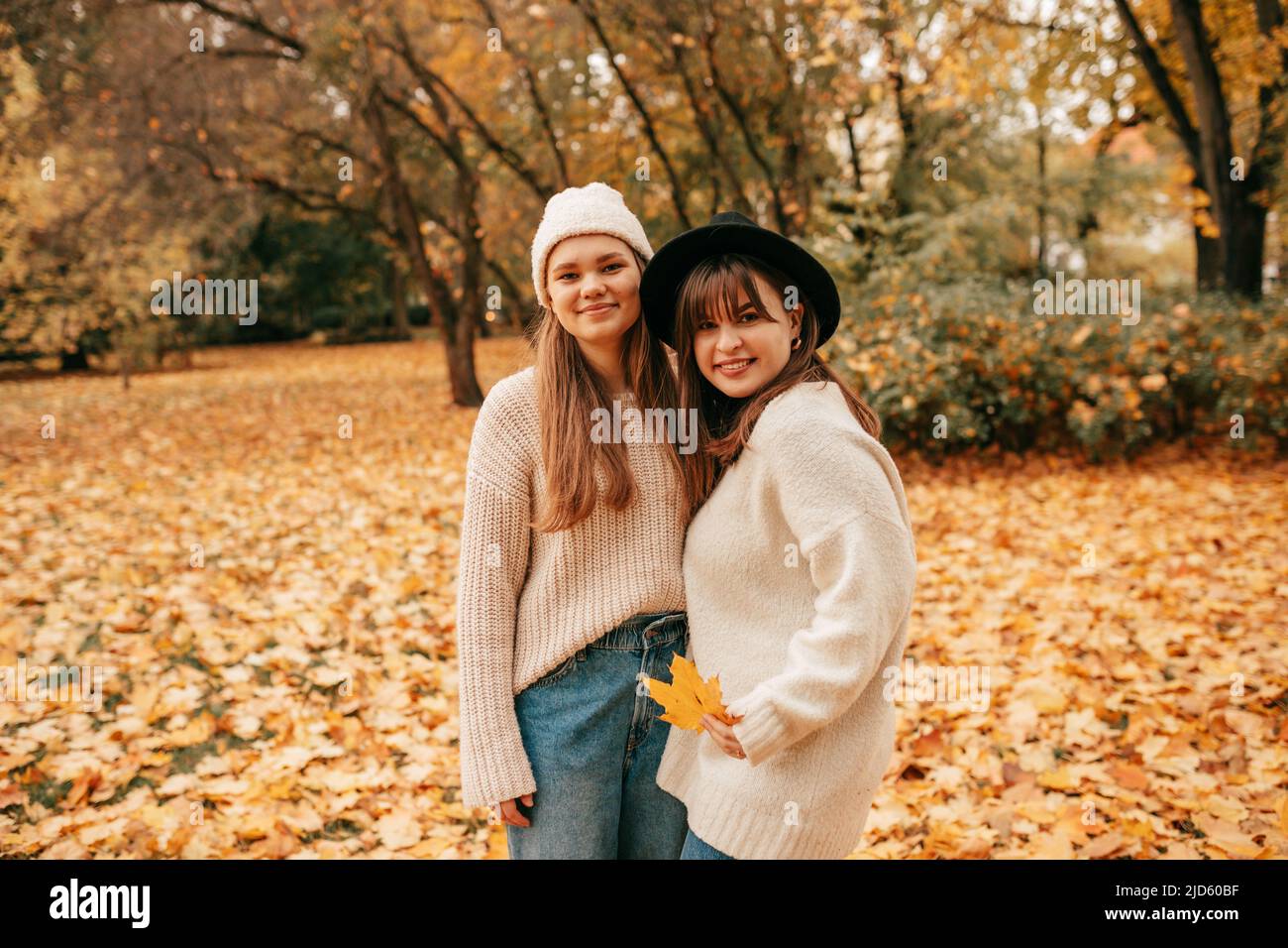 Female friendship. Portrait of autumn time in park among pile of fallen leaves of two happy young women standing embracing. Fun vacation. Weekend Stock Photo