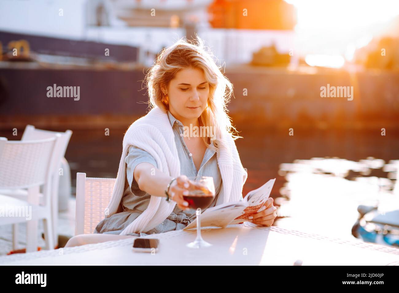 Portrait of young thoughtful gorgeous woman with long hair, wearing blue shirt, white sweater, sitting at white table. Stock Photo