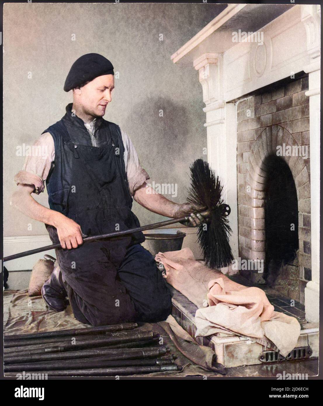 A chimney sweep kneels on the hearth and prepares to insert his brush up the chimney. Colourised version of : 10108873       Date: 1940s Stock Photo