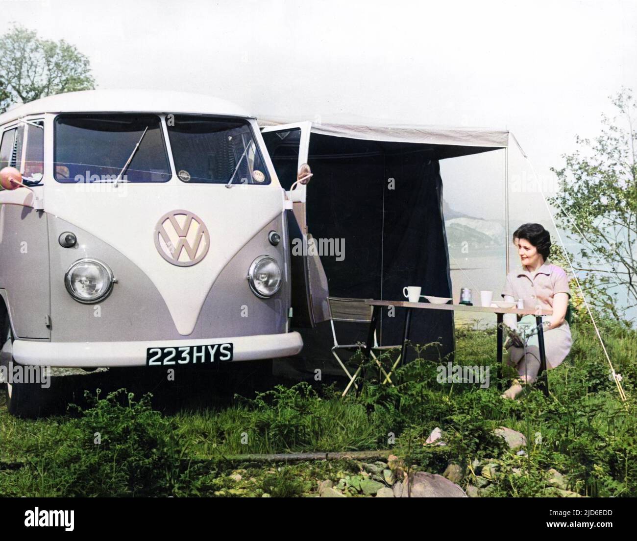 A woman demonstrates how convenient it is to have one's breakfast in the Great Outdoors, with the marvellous VW Camper Caravan. Colourised version of : 10144303       Date: 1963 Stock Photo