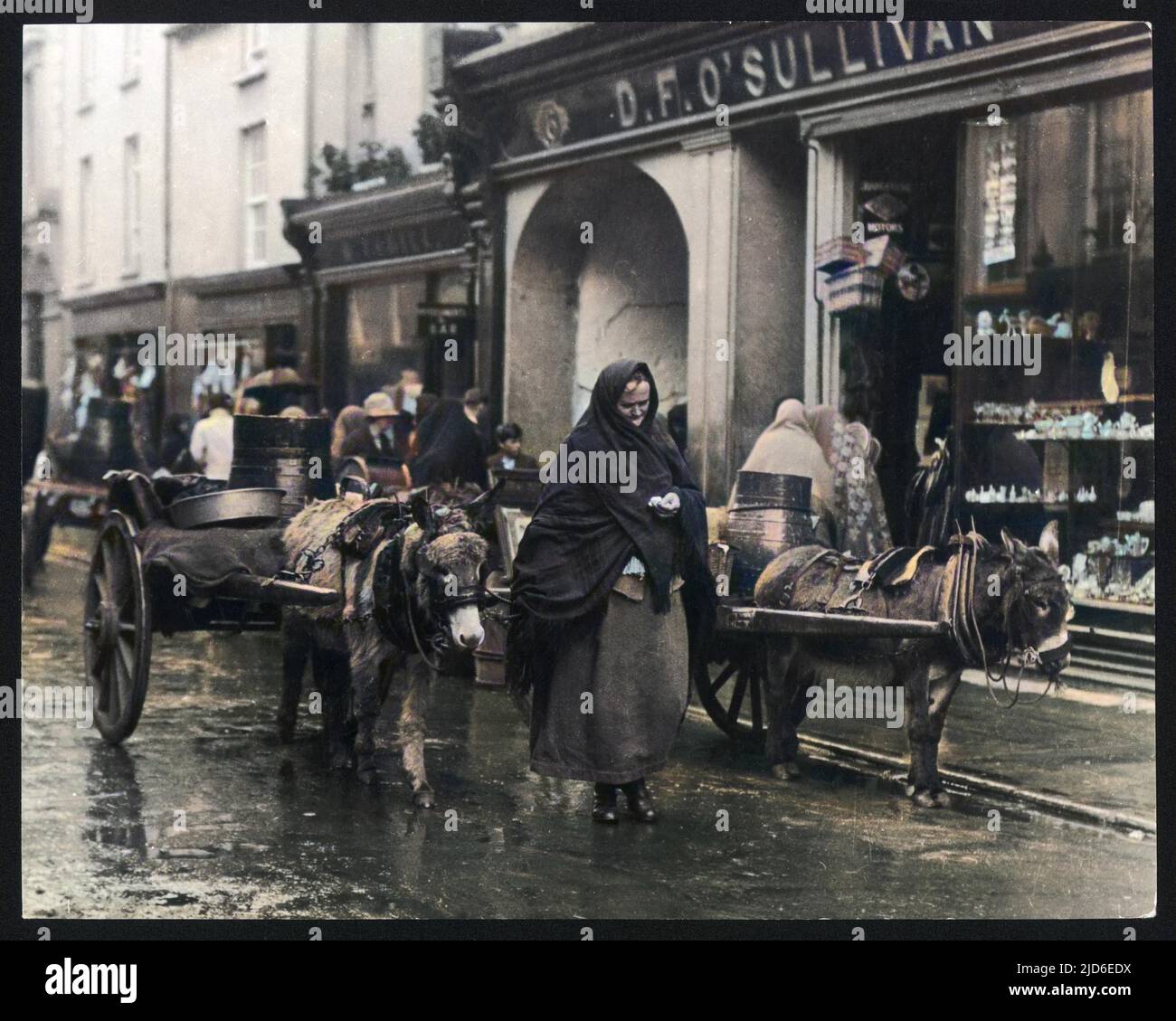 An old woman with a donkey cart counts her change whilst walking through the rainy streets of Killarney, Co. Kerry. Colourised version of : 10136876       Date: 1940s Stock Photo