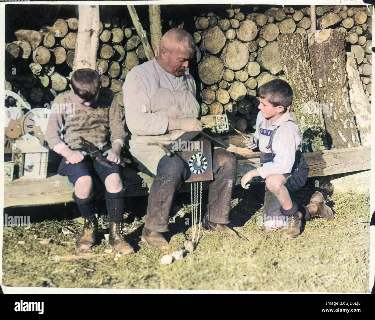 Two little boys help an old clockmaker, perhaps their grandfather, to make a cuckoo clock in the Black Forest, Germany. Colourised version of : 10155071       Date: 1930s Stock Photo