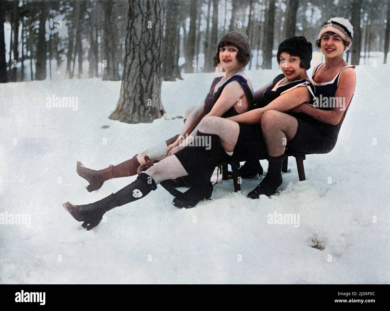 Three saucy girls on a sledge showing a 'bit of leg'! Colourised version of : 10162011       Date: early 1930s Stock Photo