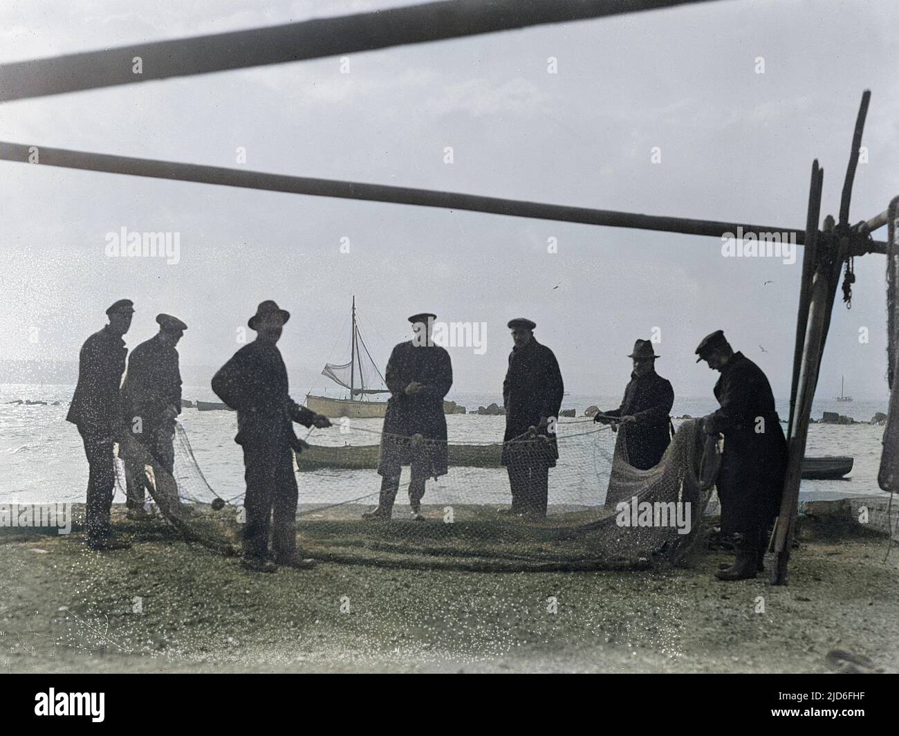 A group of fishermen on the beach at Margate, Kent, England, sorting their fishing nets. Colourised version of : 10165182       Date: early 1930s Stock Photo