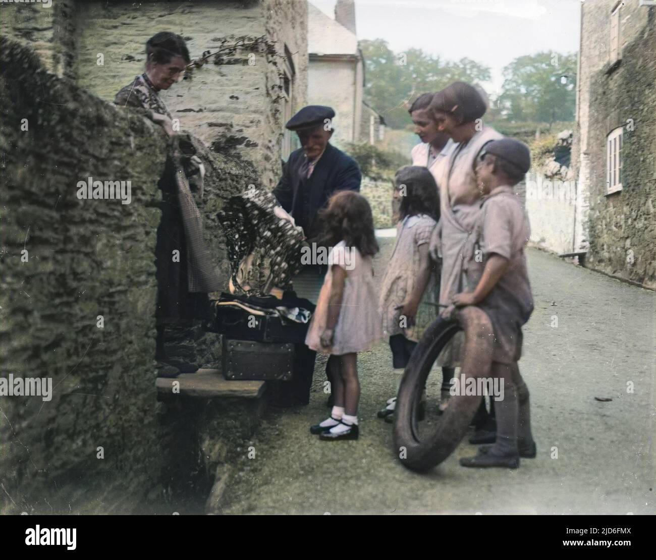 Mothers and children gather around the local rag and bone man with their various offerings on the back streets of Harbertonford, south Devon, England. Colourised version of : 10167335       Date: early 1930s Stock Photo