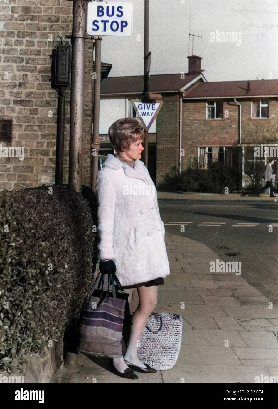 A young pregnant woman waiting at a bus stop with her shopping bags. Colourised version of : 10170945       Date: 1960s Stock Photo