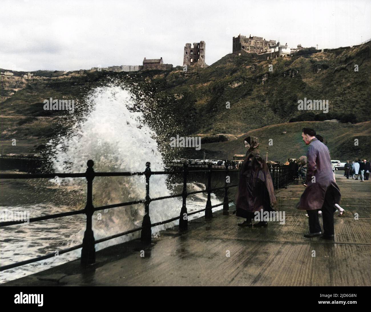 Rough sea and waves lashing the Yorkshire coastline at Scarborough, England, much to the delight of wet holidaymakers! Colourised version of : 10171840       Date: 1950s Stock Photo