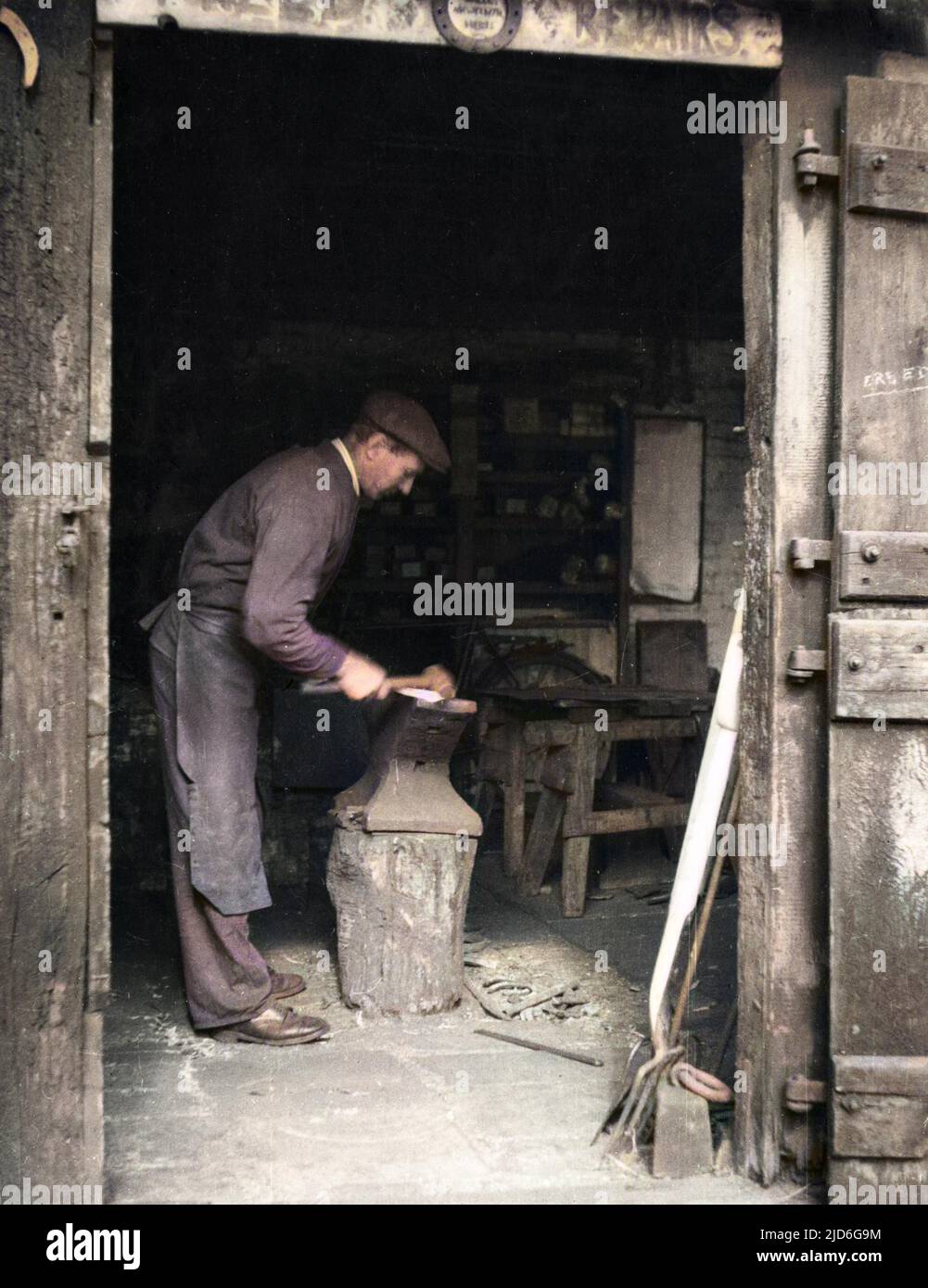 The Smithy (blacksmith) at work beneath the shadow of the busy railway viaduct which runs through the village of Digswell, Hertfordshire, England. Colourised version of : 10180298       Date: 1930s Stock Photo