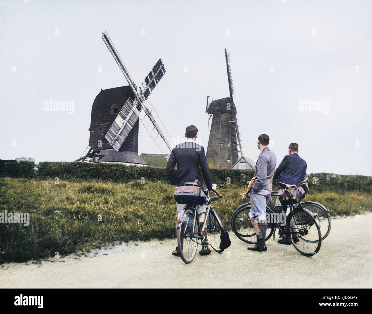 Three men cyclists admire the the two windmills at Outwood, Surrey, England. The left one was built in 1665 and still stands today. The right, built 1790, blew down in a gale 1960 Colourised version of : 10170957       Date: Oct-38 Stock Photo